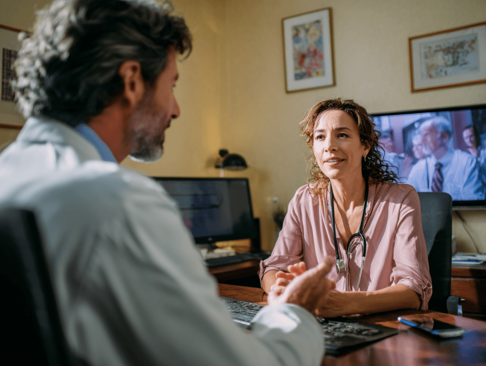 Two clinicians in conversation across a desk in a consulting room