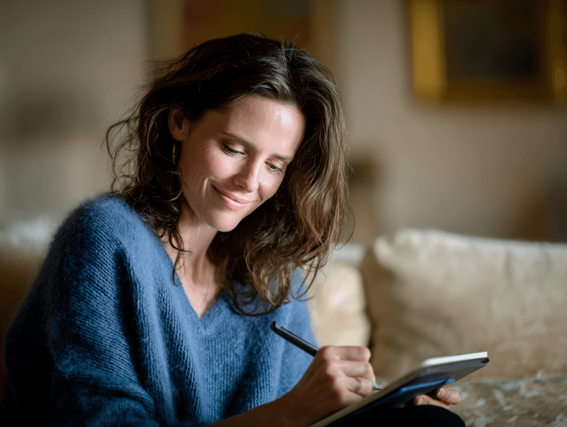 A woman in a blue jumper writing in a notebook at home