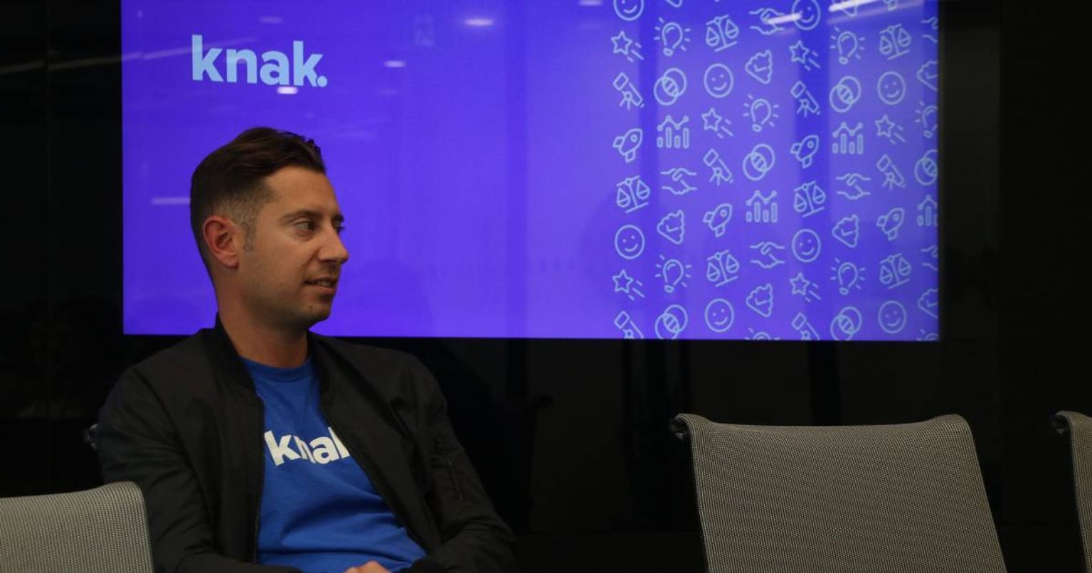 Pierce Ujjainwalla sitting in front of a blue screen with Knak logo