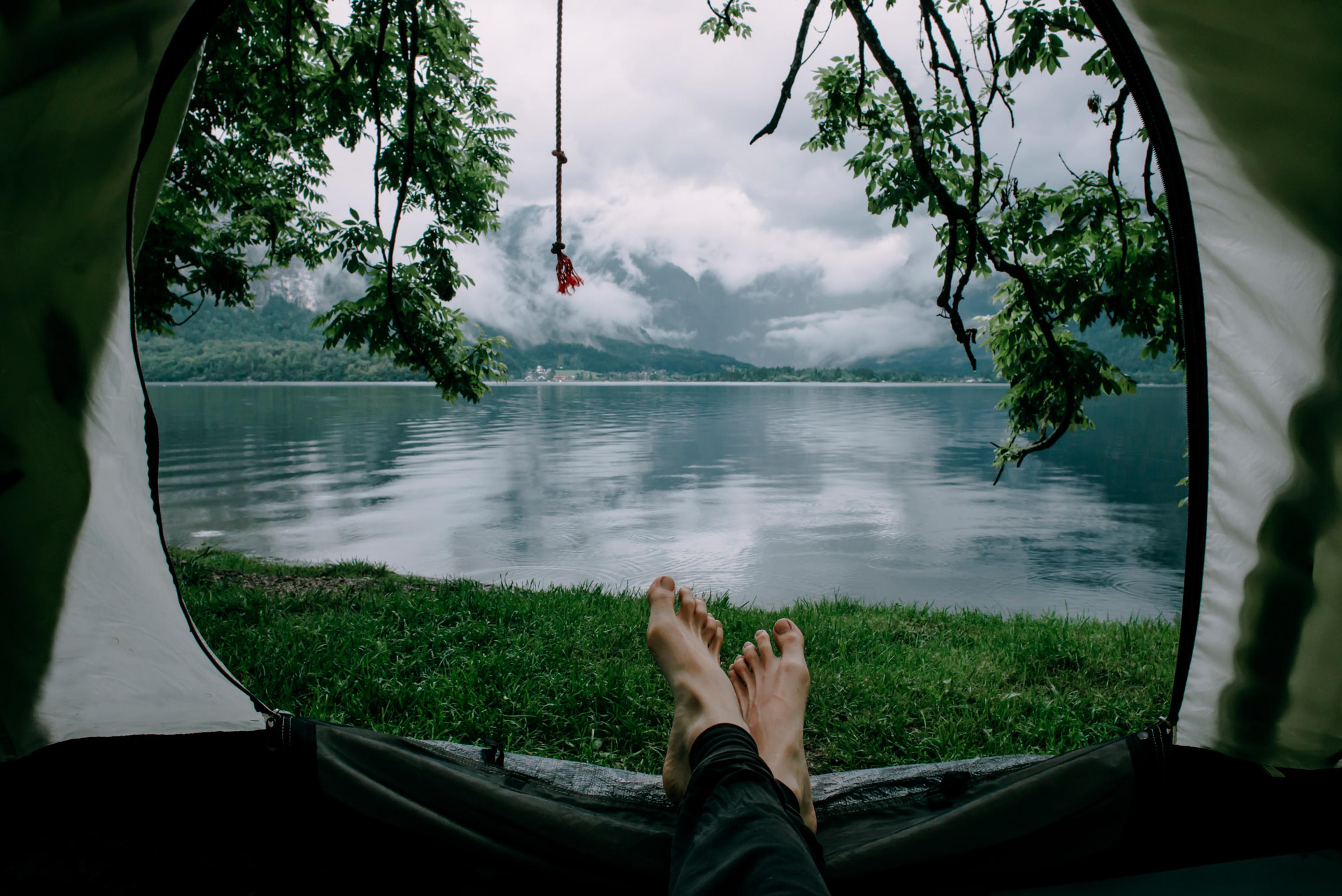 View out of a tent looking out towards a lake surrounded by mountains, with the feet of a person  in the foreground