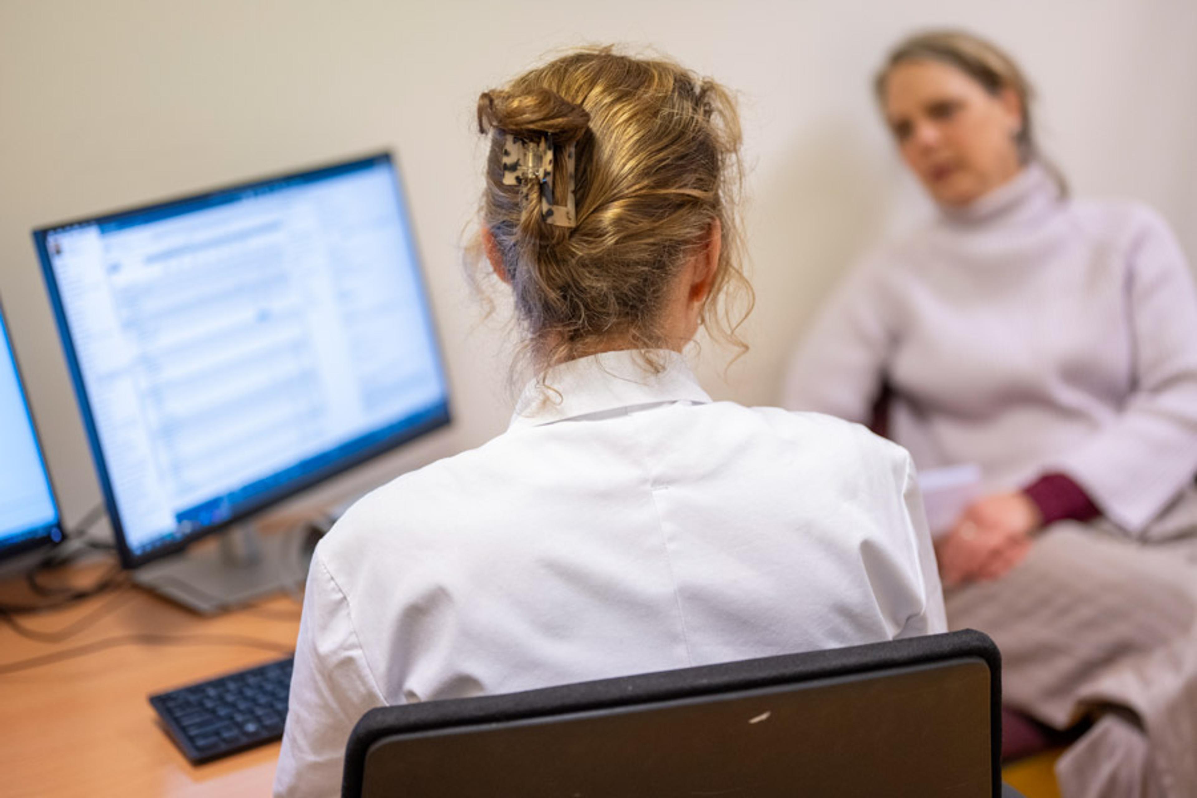 Kvinnlig läkare som sitter vid en datorskärm med en kvinnlig patient bredvid