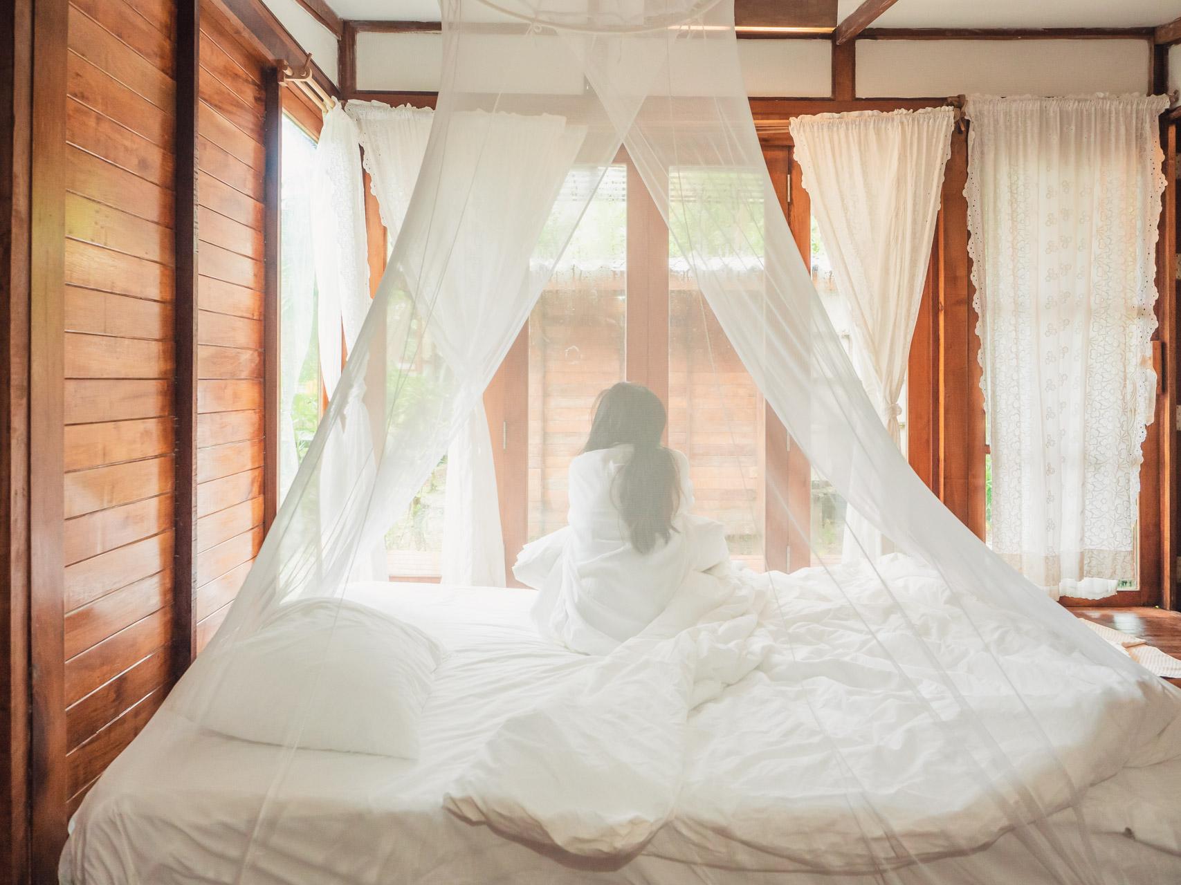 Woman sat on a bed underneath a mosquito net