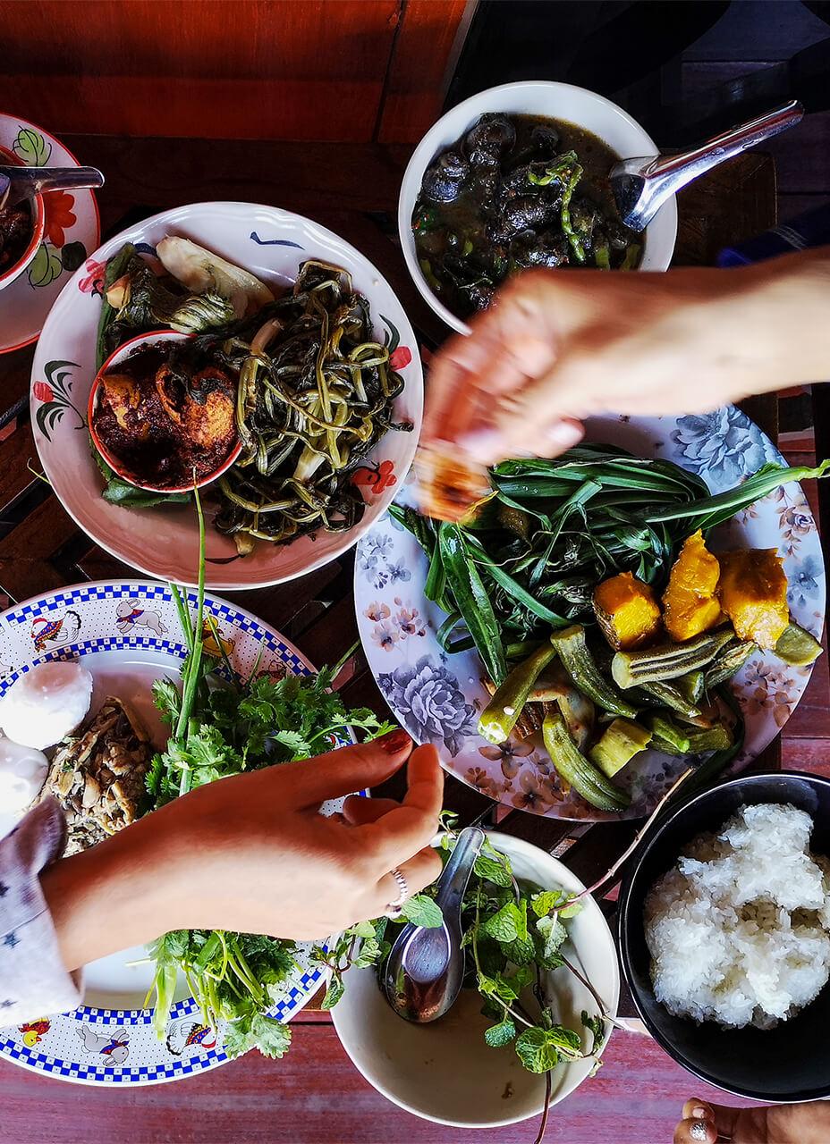 A top down view of a table filled with plates containing a variety of healthy dishes with hands shown sharing food
