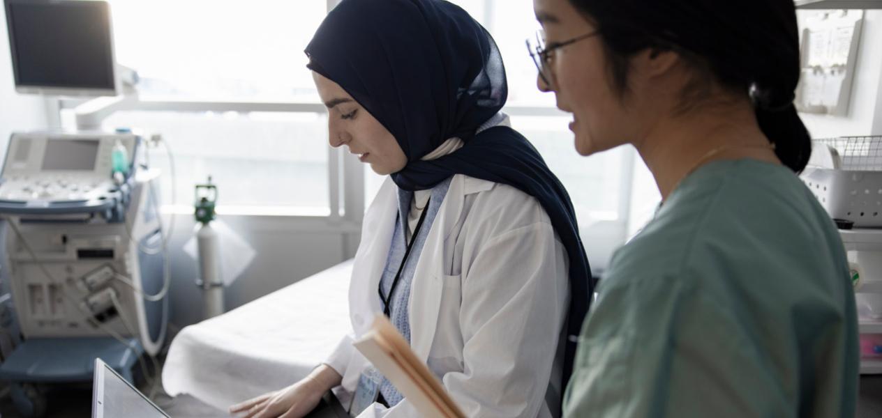Two female healthcare professionals in a hospital room looking at patient results on a clipboard