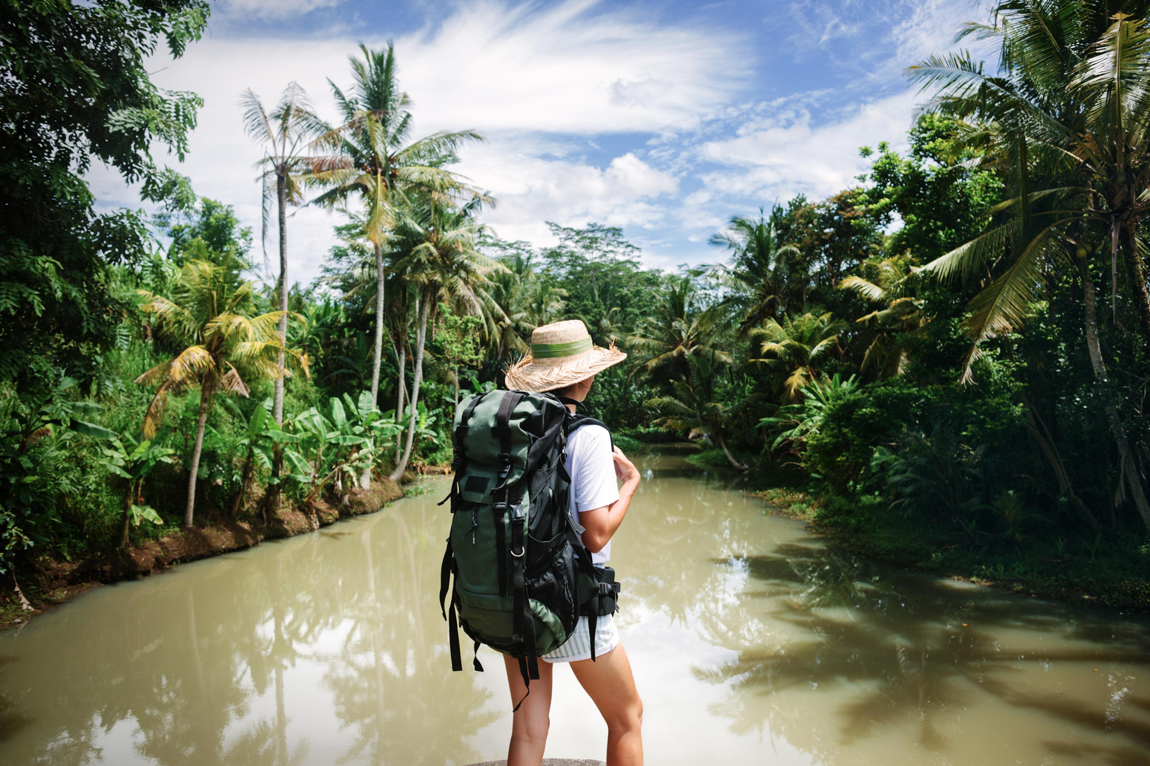 Person in a hat with a backpack looking out towards a swampy setting stood next to murky water