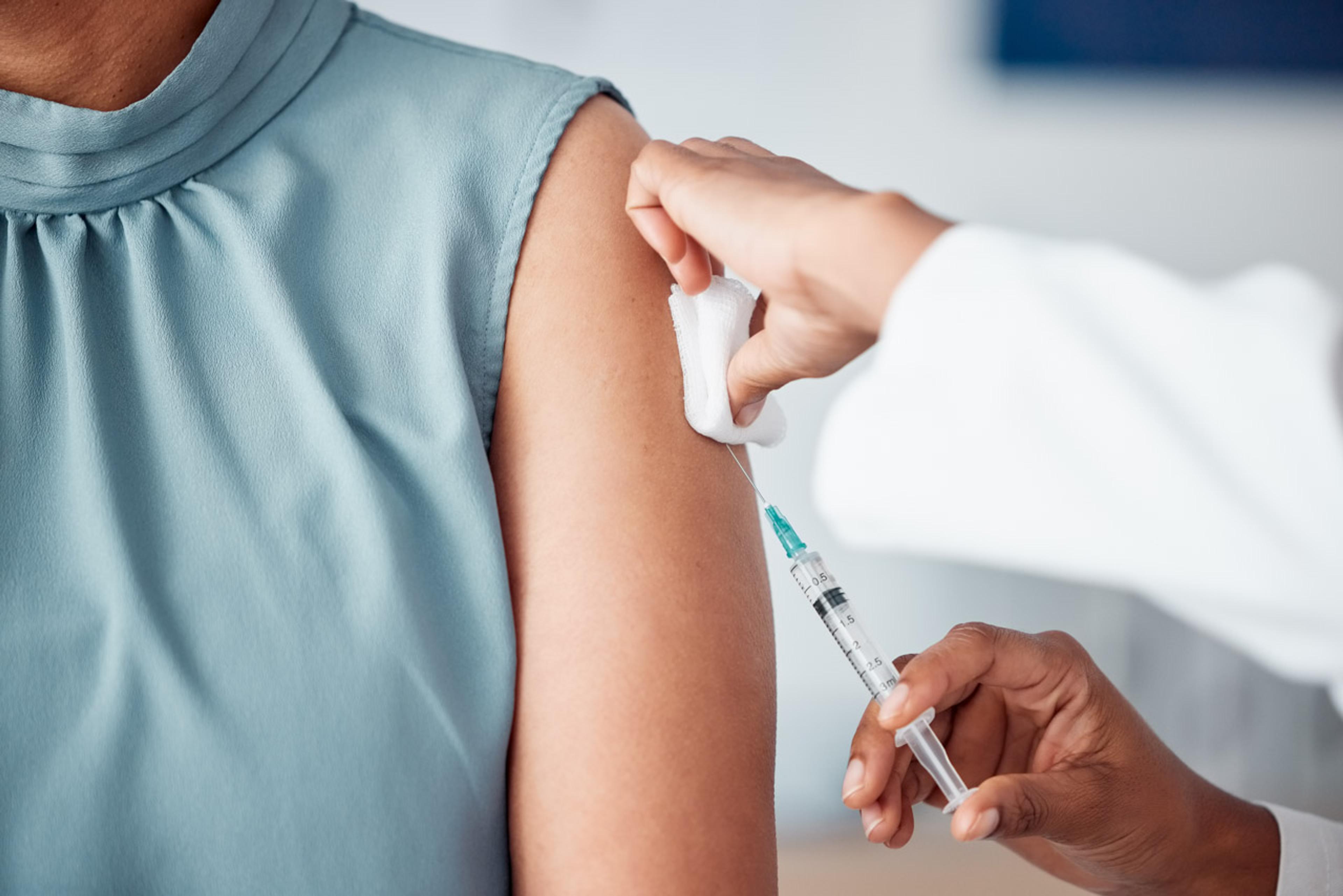 Woman in blue top receiving a vaccine in her arm by a female nurse