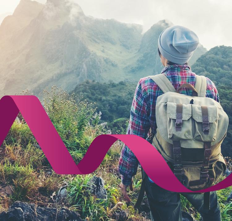 Hiker standing with their back to the camera looking towards a mountain range wearing a backpack
