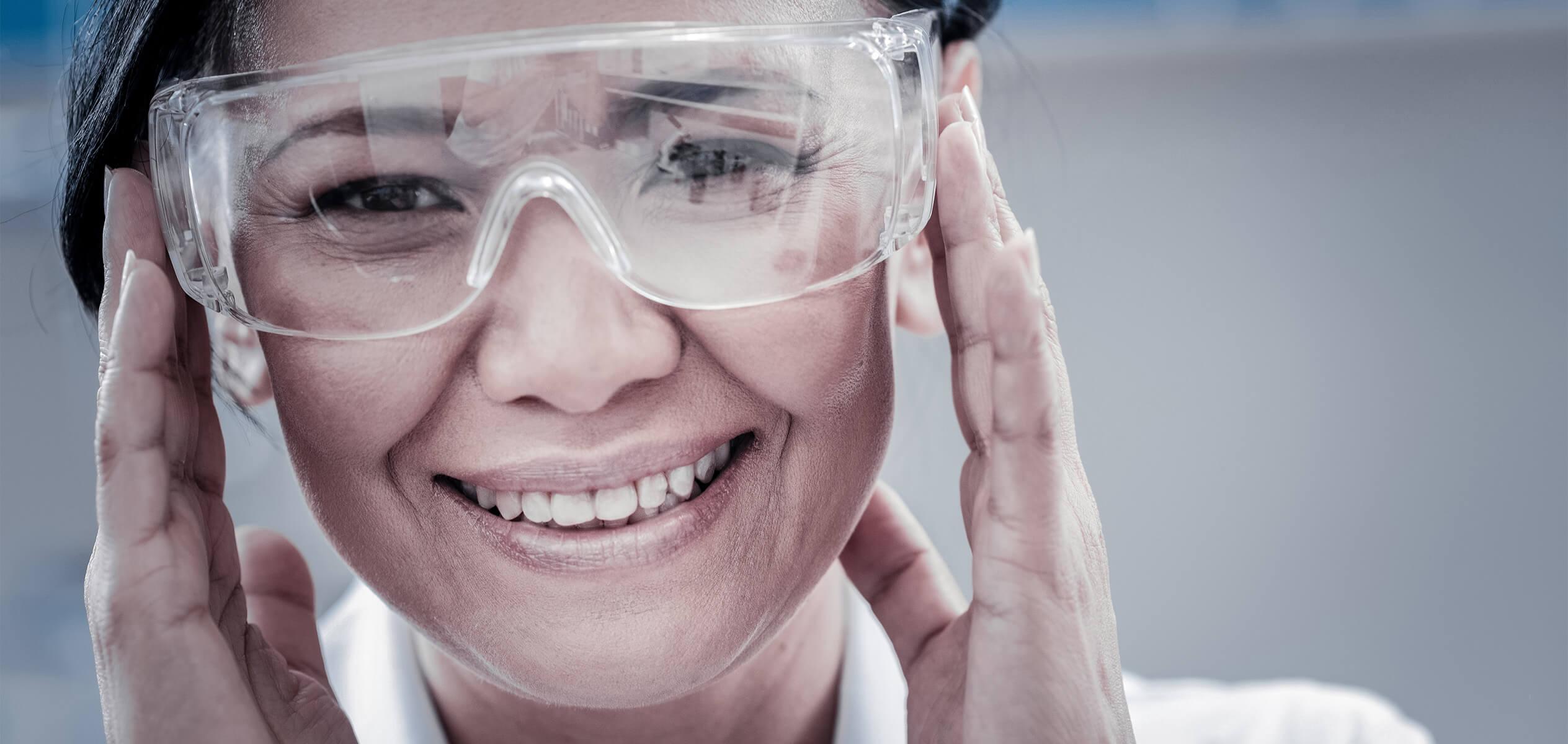 Smiling female scientist with safety glasses holding hands against face