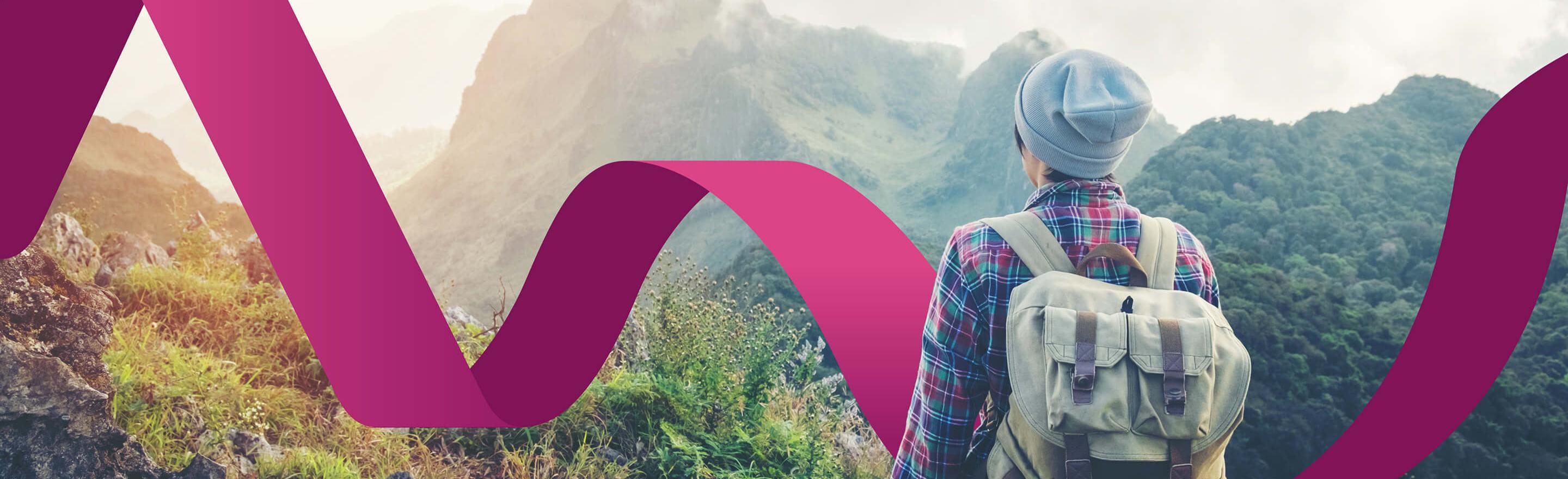 Hiker standing with their back to the camera looking towards a mountain range wearing a backpack