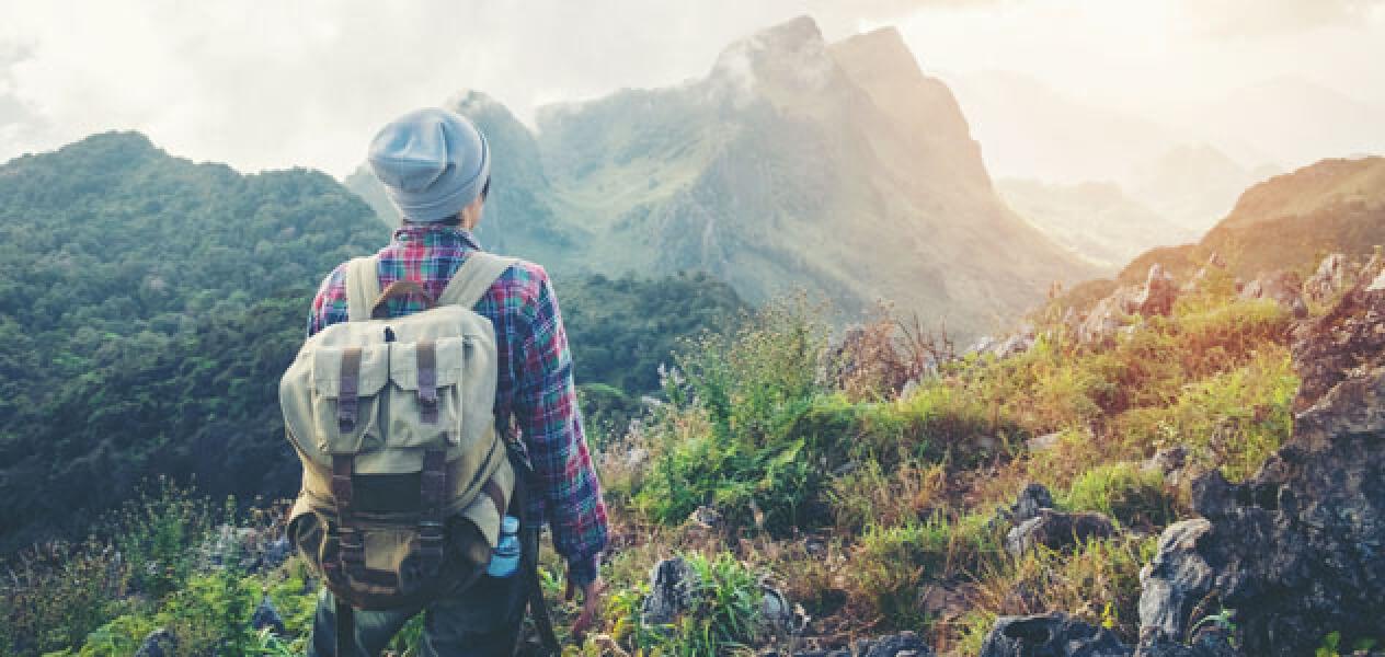 Hiker standing with their back to the camera looking towards a mountain range wearing a backpack