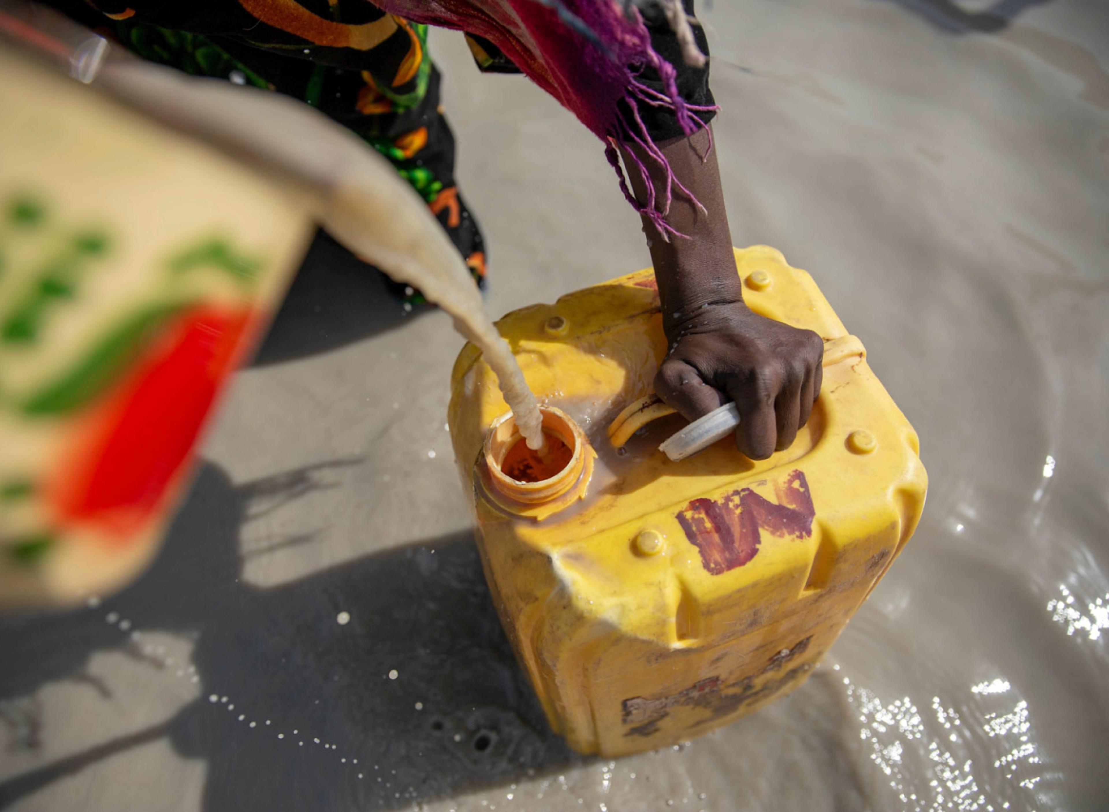Close up of a person pouring murky water into a large yellow container