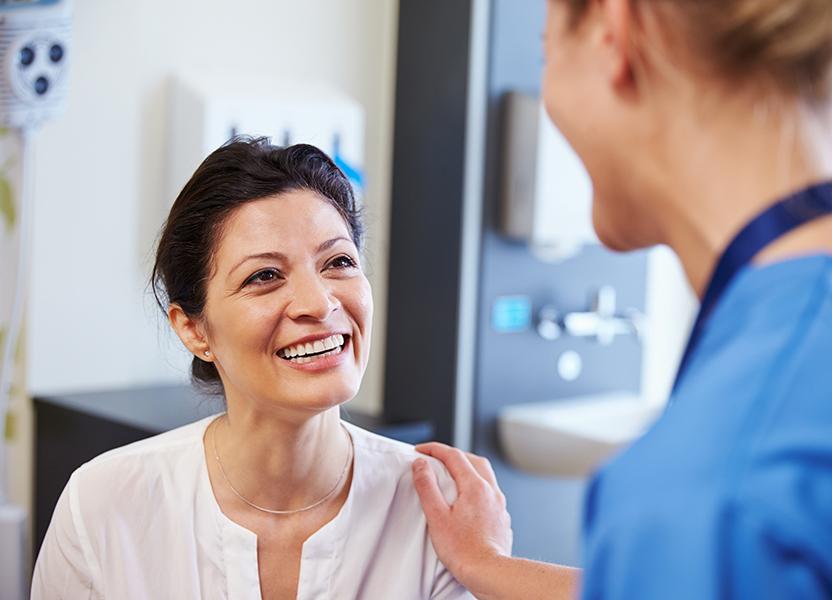A healthcare professional with their hand on the shoulder of a smiling female patient