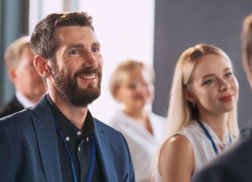 Man smiling in between a group of people attending a congress wearing a lanyard