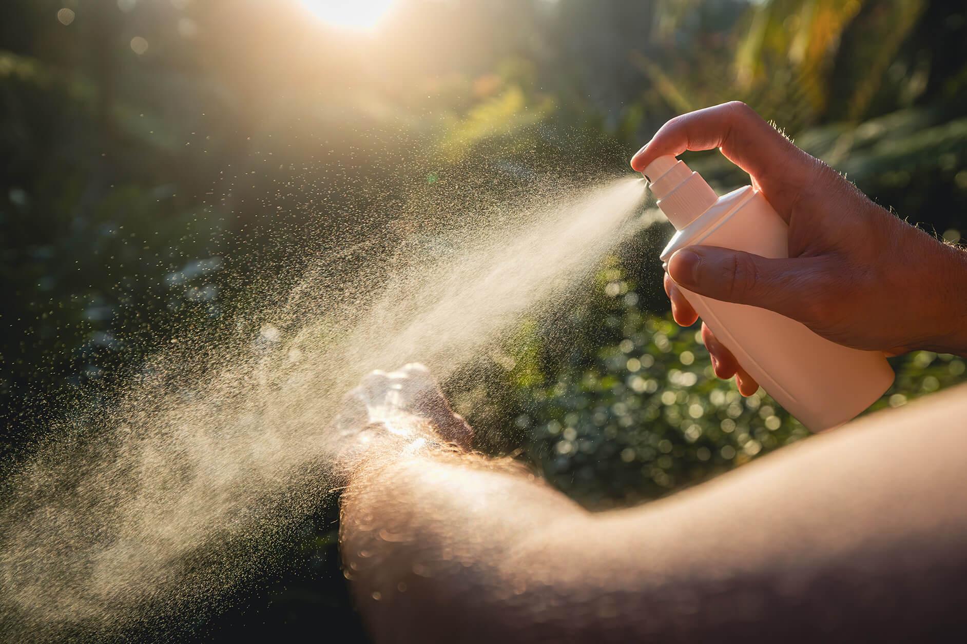 Close up on a person spraying mosquito repellant on their arm