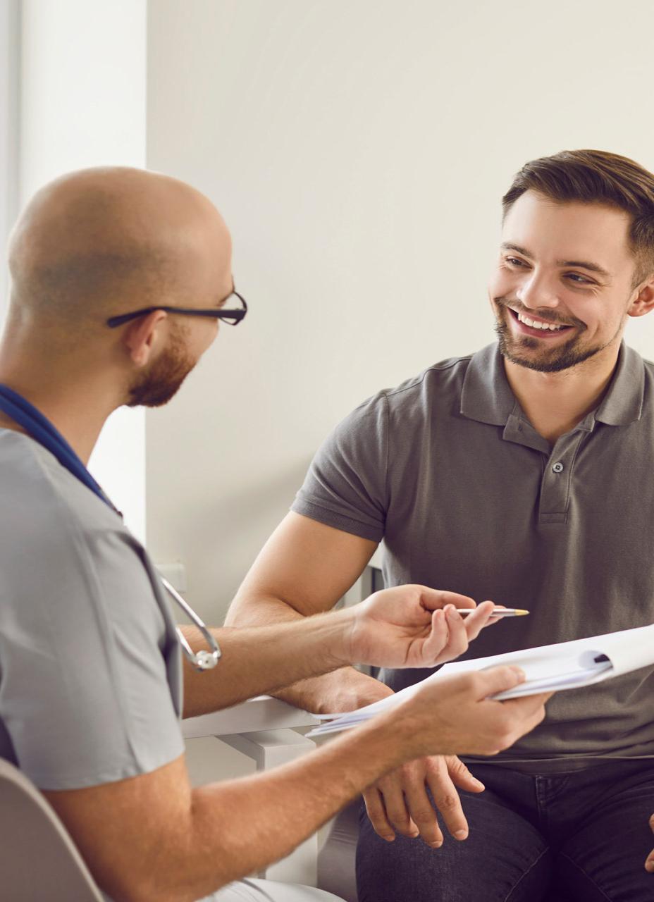 Male healthcare professional holding a clipboard talking to a smiling patient
