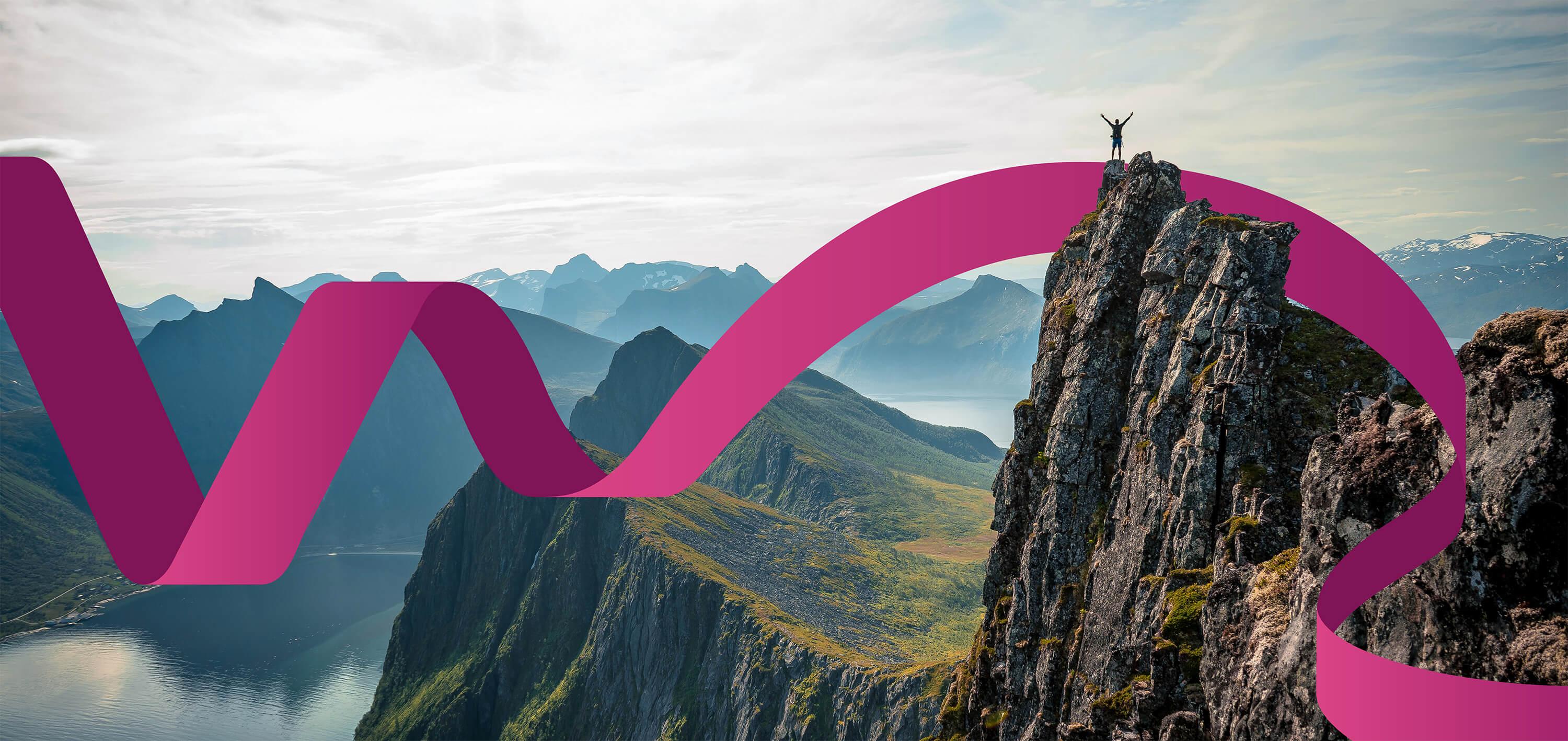 Hiker stands on a mountain top in the middle of a mountain range with a small lake below
