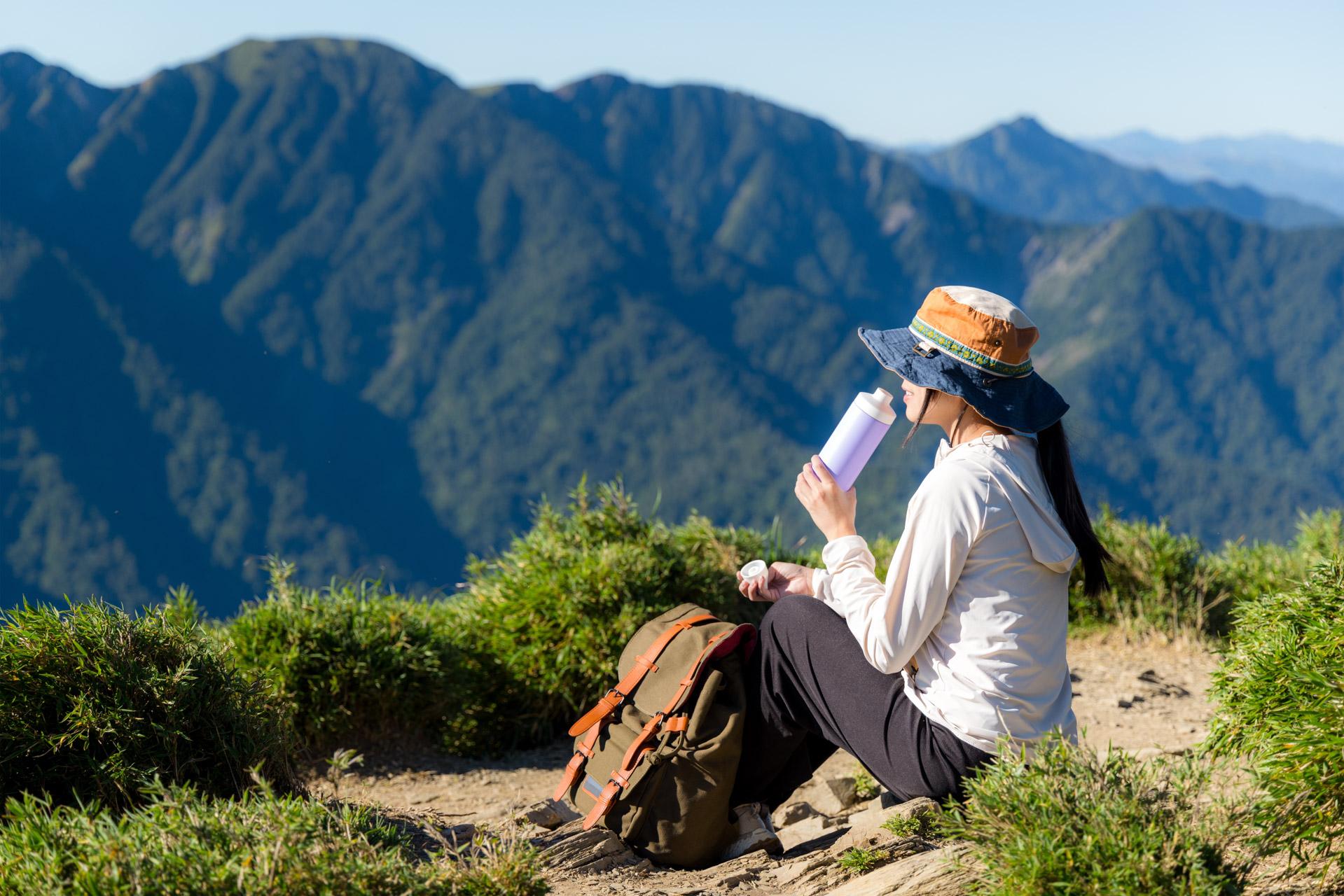Female hiker sat on a mountain edge drinking out of a bottle