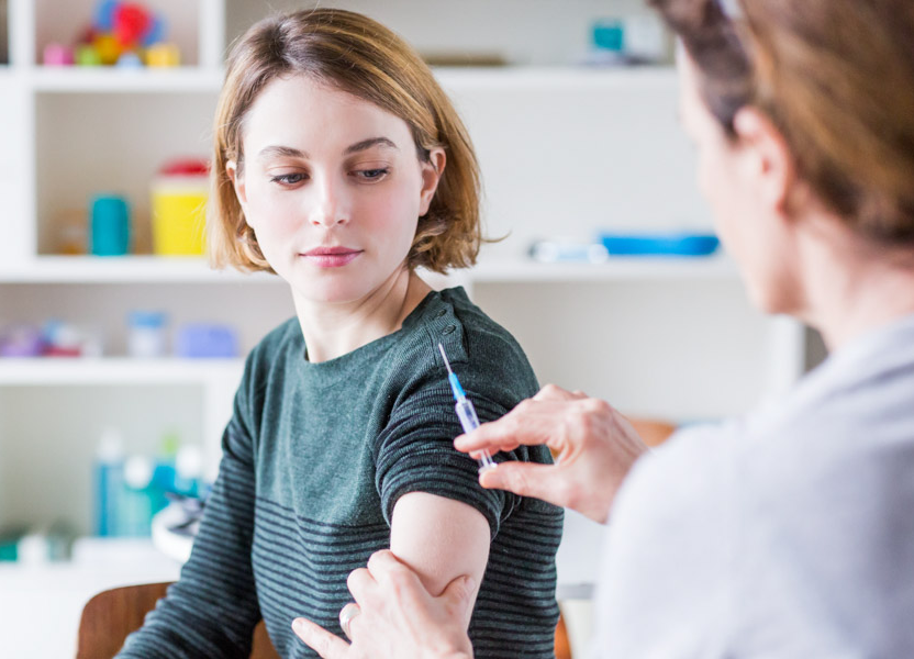 En ung kvinna ska få en injektion i armen av ev kvinnlig sjuksköterska