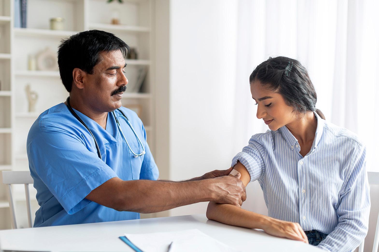 Male healthcare professional applying a plaster to a young woman’s arm