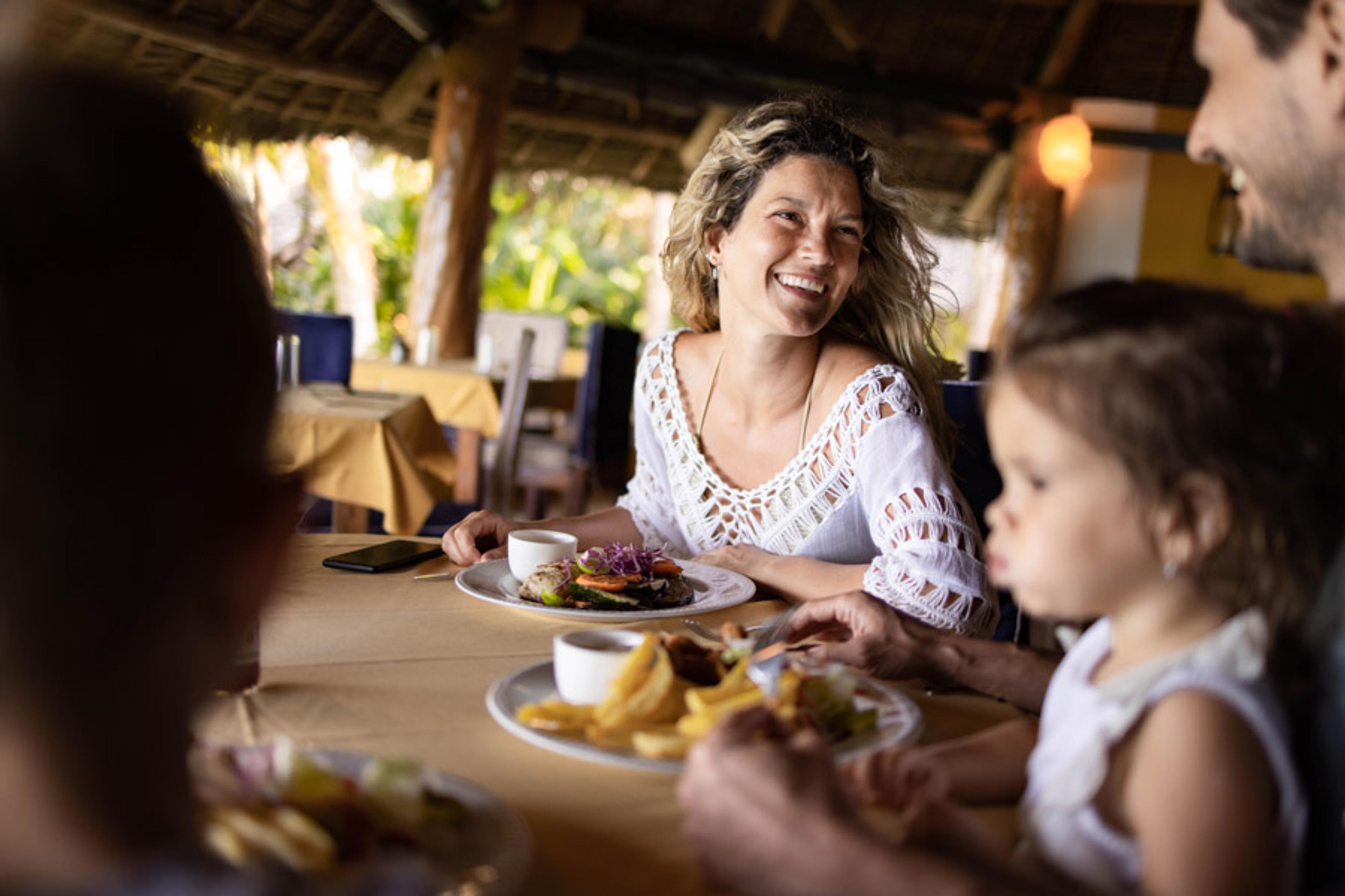 Woman laughing sat by a table  with two plates of food on the table next to a man and young child