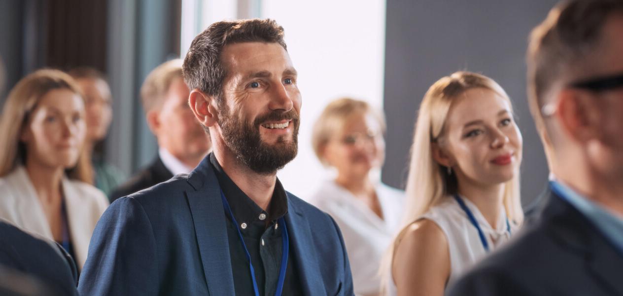 Man smiling in between a group of people attending a congress wearing a lanyard