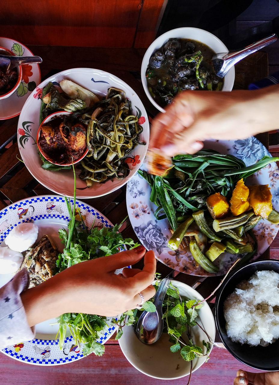 A top down view of a table filled with plates containing a variety of healthy dishes with hands shown sharing food