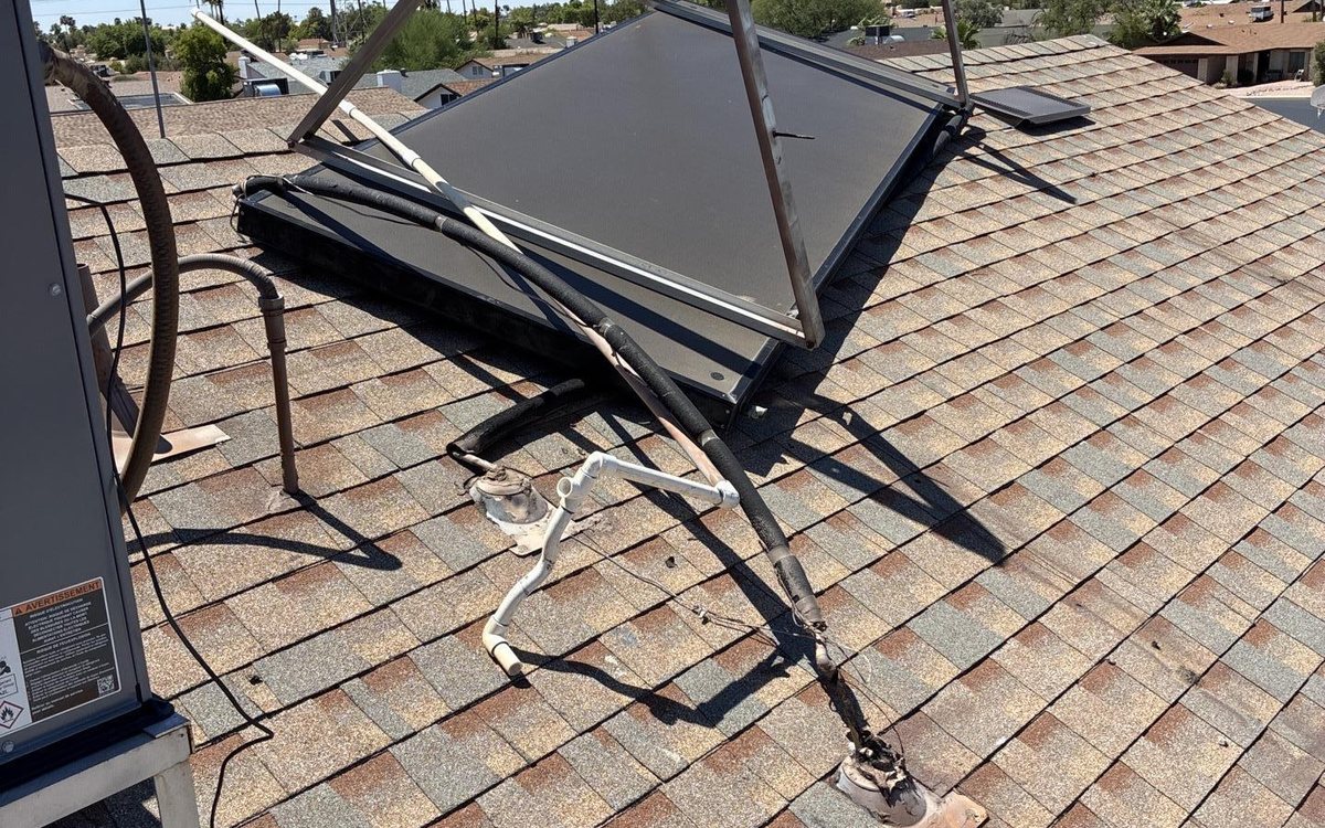 Solar panel torn loose and hanging from a shingle roof after a microburst, with the condensate line pulled away