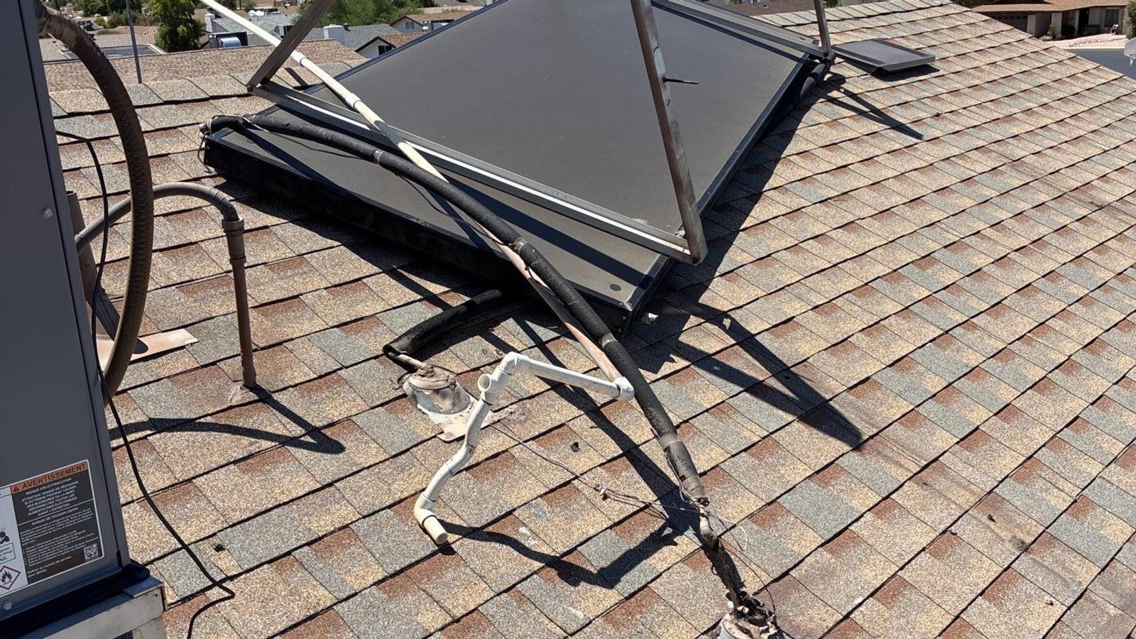 Solar panel torn loose and hanging from a shingle roof after a microburst, with the condensate line pulled away