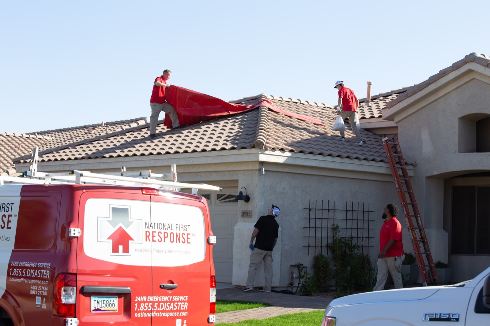 Technicians installing an emergency red tarp across a damaged tile roof