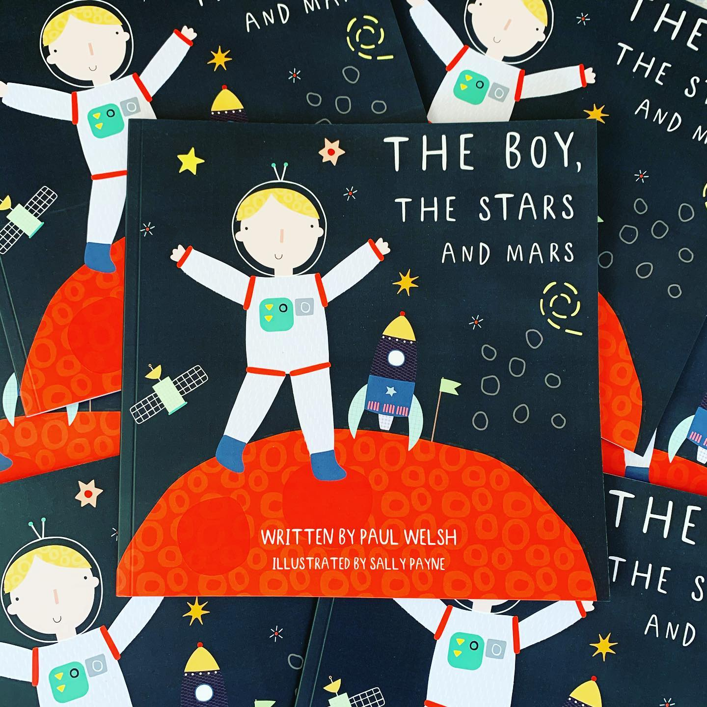 Several copies of the children's book "The Boy, The Stars And Mars," featuring a cartoon astronaut boy on a red planet with a rocket and stars.