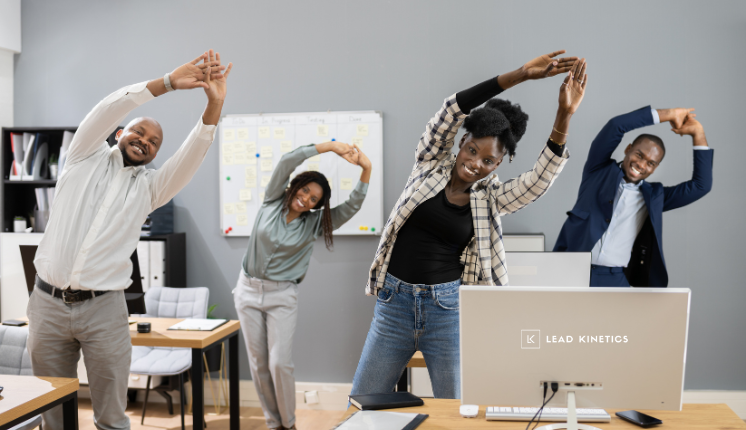 Four smiling colleagues stretching their arms above their heads in a bright office.