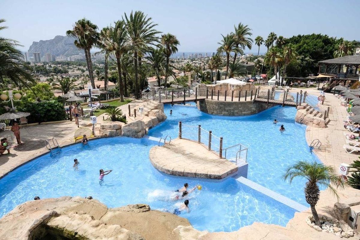 Buitenzwembad bij een woning in Calpe, omringd door palmbomen en zonnebaders, met een levendige sfeer.