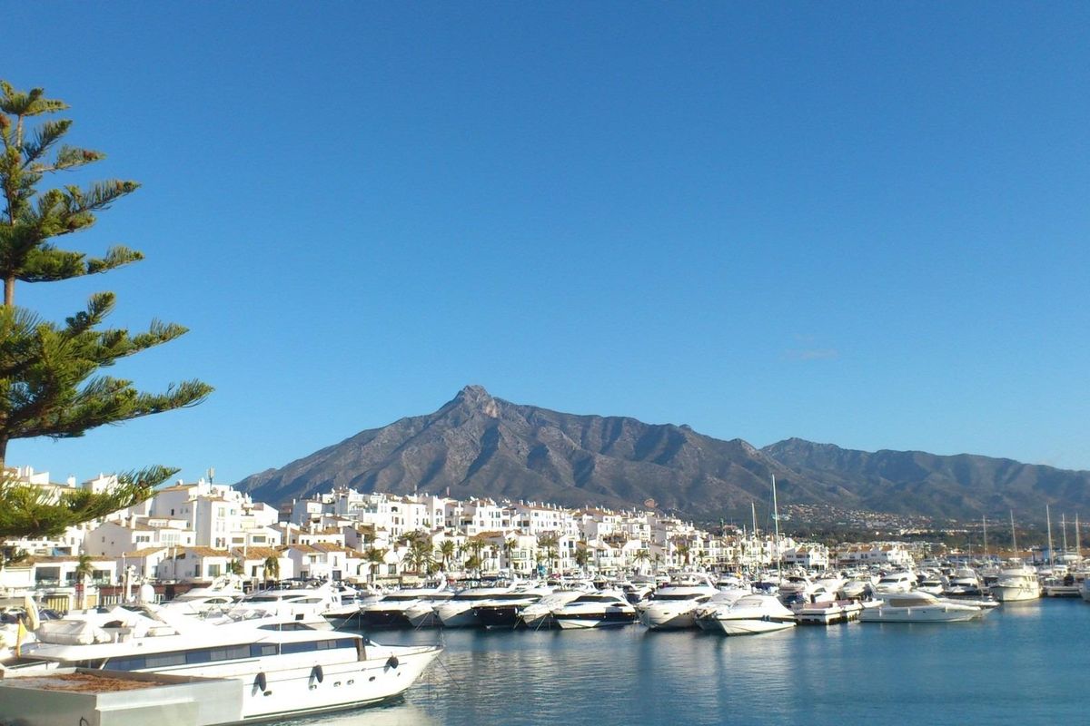 Sfeervol uitzicht op de jachthaven met luxe jachten en een pittoresk berglandschap in Marbella, Costa del Sol.