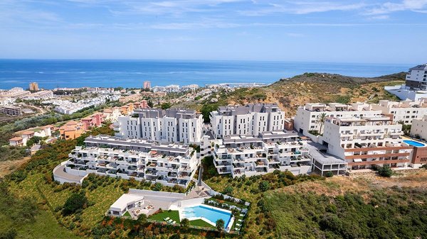 Luchtfoto van een 3-slaapkamer appartementcomplex in Manilva, Costa del Sol, omgeven door heuvels en de oceaan.