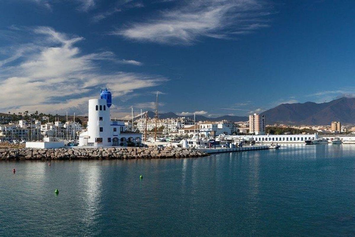 Panoramisch uitzicht op de jachthaven van Manilva met boten en een vuurtoren, dat de kust schoonheid benadrukt.