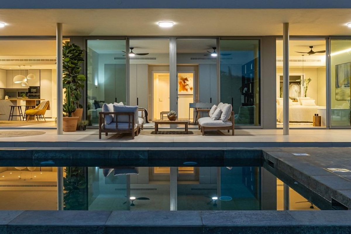 Verlichte zwembadruimte in de avond met de woonruimte zichtbaar in een appartement in Fuengirola.