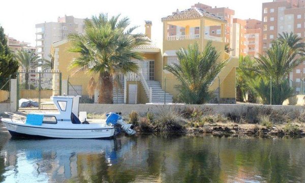 Buitenaanzicht van een villa met palmen en een boot op het water in La Manga del Mar Menor, Spanje.