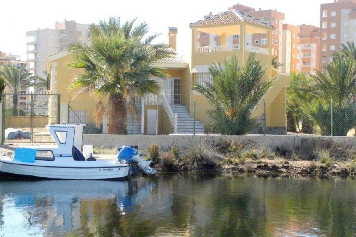 Buitenaanzicht van een villa met palmen en een boot op het water in La Manga del Mar Menor, Spanje.