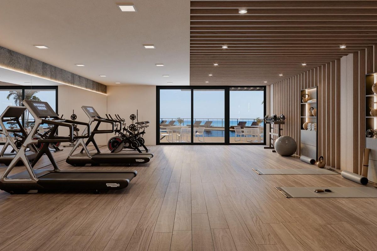 Moderne fitnessruimte in Mijas, uitgerust met fitnessmachines en grote ramen met uitzicht op het zwembad.