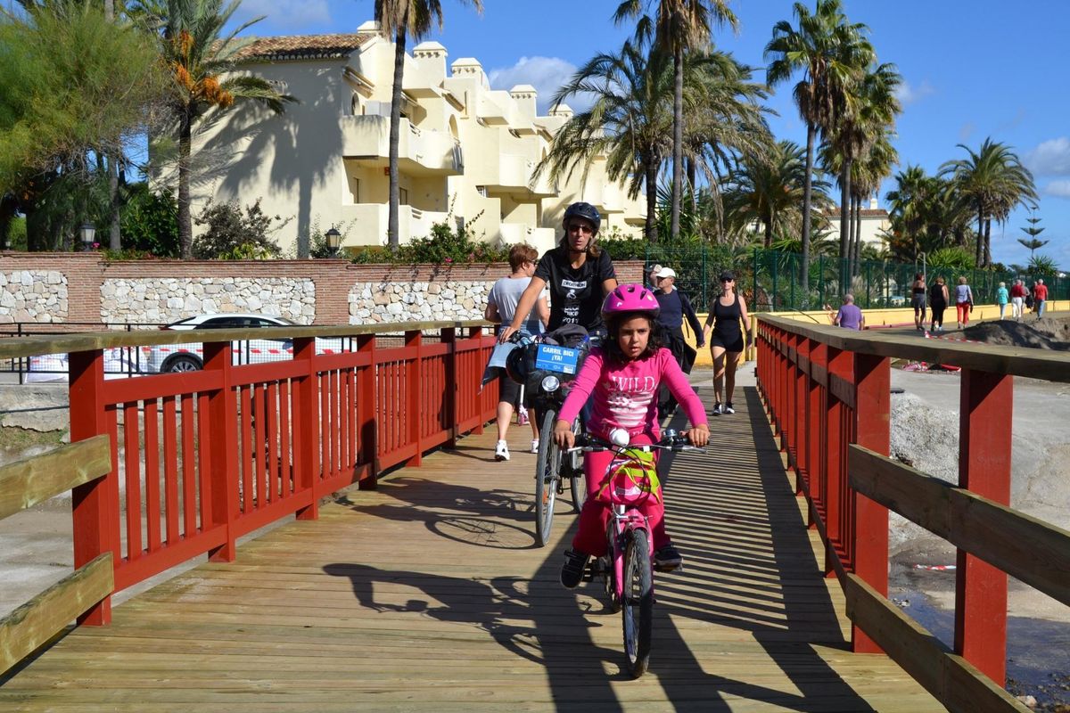 Gezin met fietsen op een houten brug nabij het strand in Mijas, Costa del Sol.