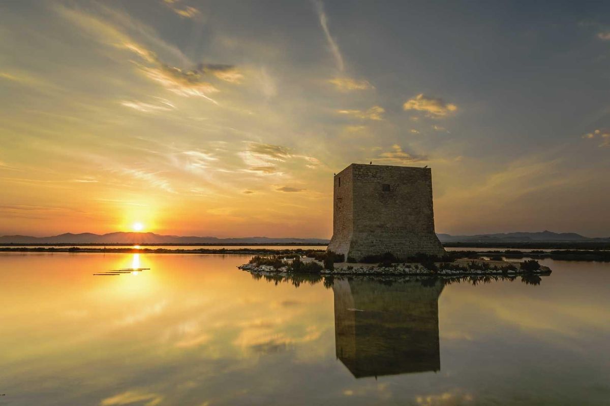Zonsondergang zicht over de rustige wateren van Santa Pola, met een historische toren die in het meer weerkaatst.