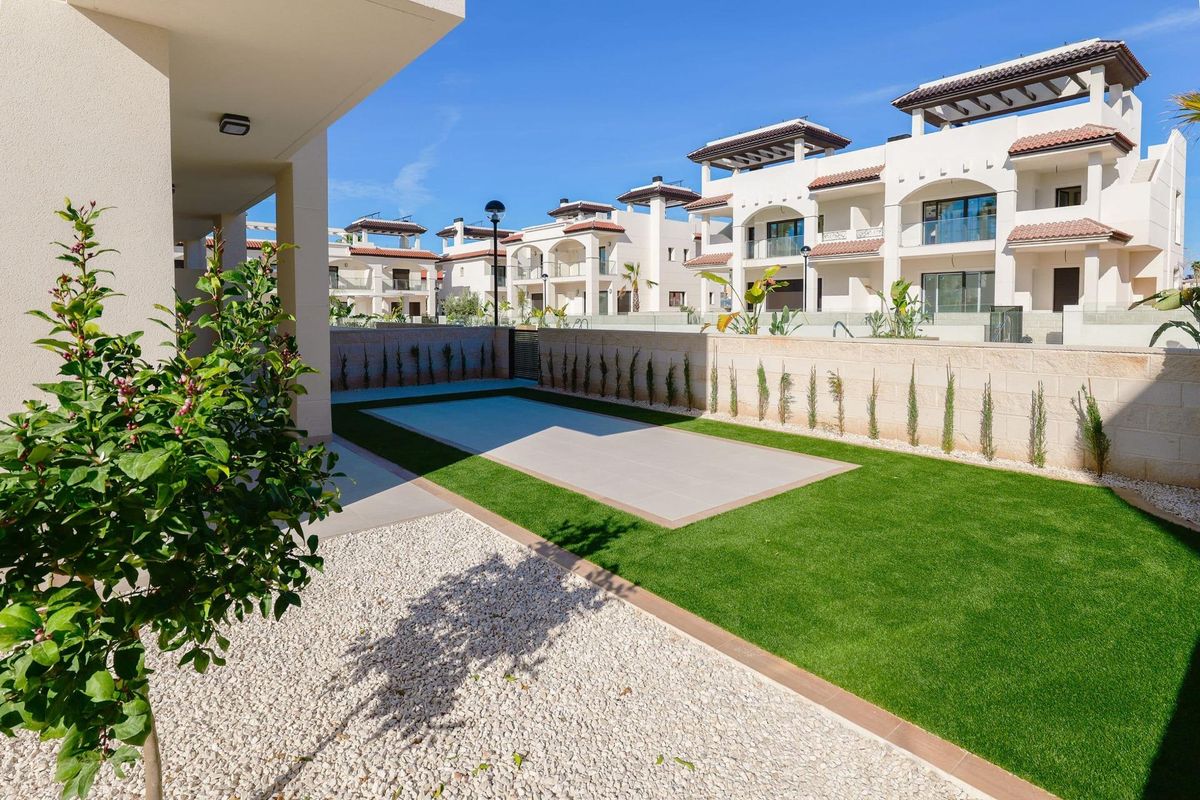 Privé tuin met gras en tegels, omringd door appartementen in Rojales, Costa Blanca Zuid.