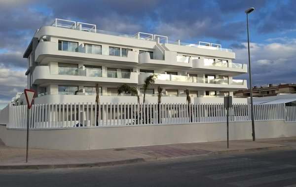 Exterior view of a modern 2-bed apartment building in Orihuela Costa, surrounded by palm trees.