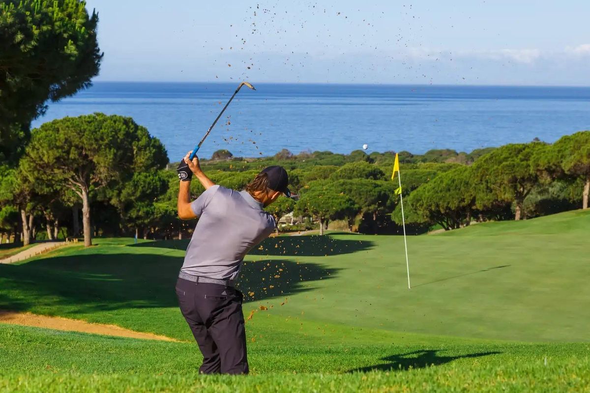 Golfspeler die slaat op een baan met uitzicht op de oceaan in Marbella, genietend van het zonnige weer.