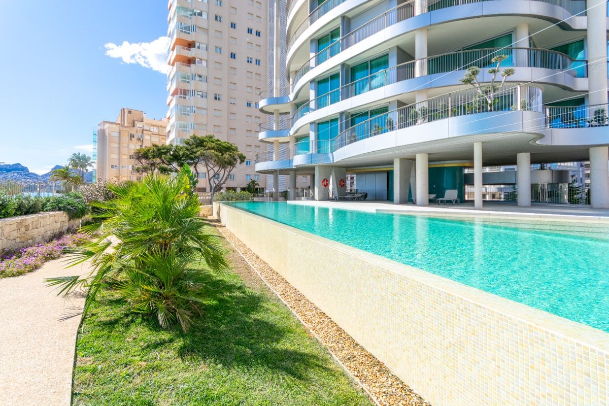 Uitzicht op het zwembad vanuit de tuin, met op de achtergrond een appartementgebouw in Calpe, Costa Blanca.