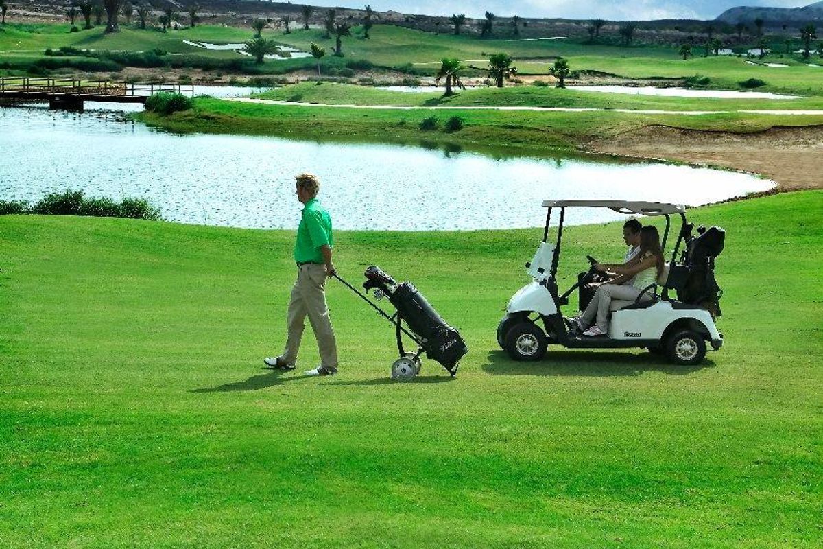Golfers wandelen met uitrusting nabij een sereen waterlichaam op een Costa Blanca golfbaan.