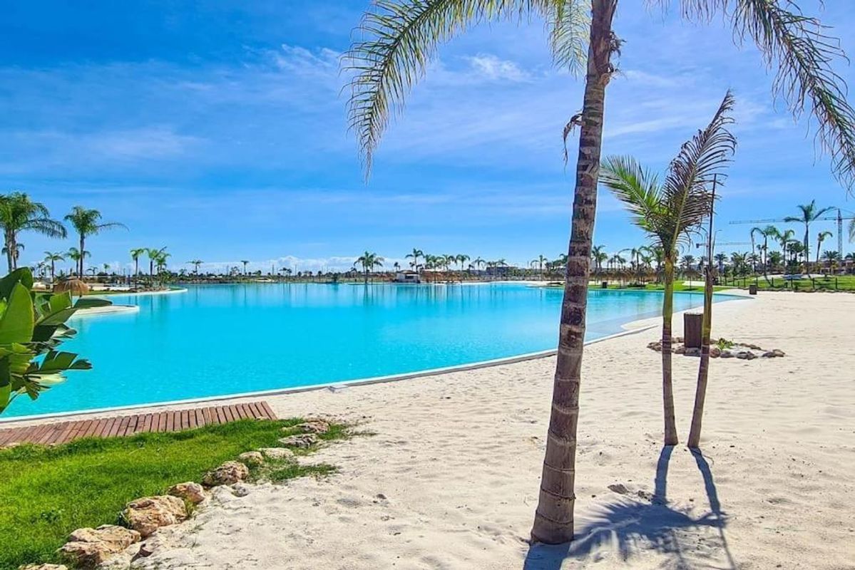 Zandstrand naast een turquoise lagune zwembad omringd door palmbomen in Torre Pacheco.