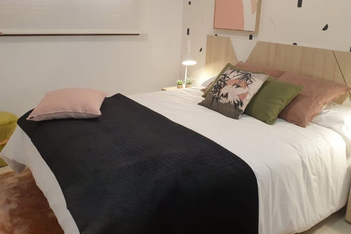 Gezellige slaapkamer met zwarte en roze accenten, houten hoofdeind en zachte verlichting in Spaans kustappartement