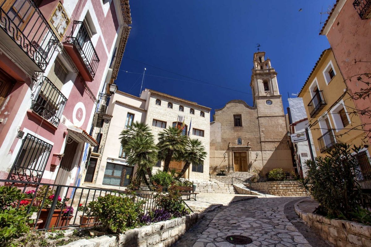 Charmante straat in Finestrat met kleurrijke gebouwen en een historische kerk onder een heldere blauwe lucht.