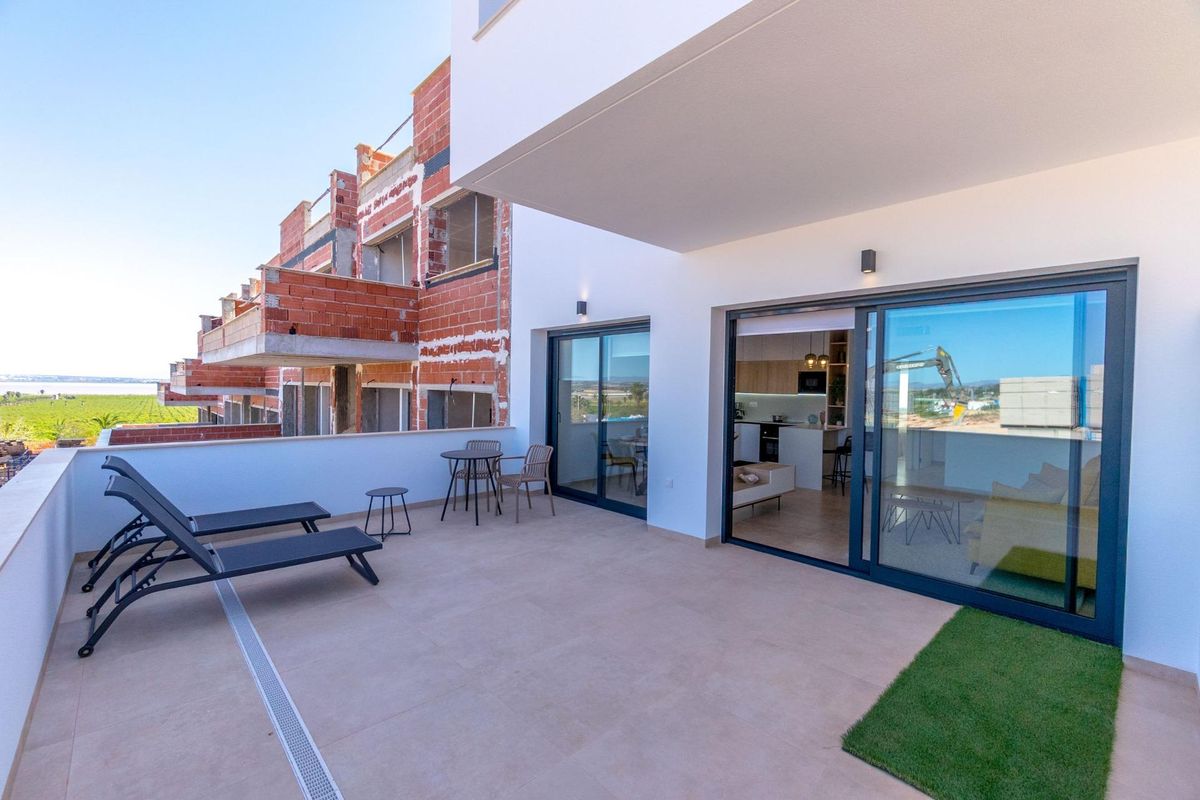 Ruim terras van een moderne bungalow nabij Torrevieja, met zitplaatsen en uitzicht op de groene omgeving.
